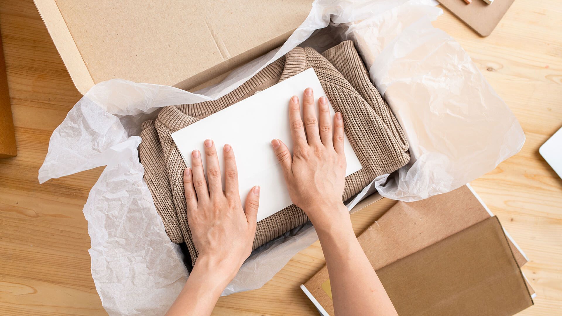 A business owner packing clothing into a parcel with sustainable packing materials like paper. 